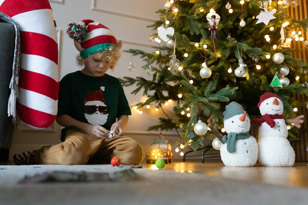 chłopiec w czapce elfa obok choinku bawi się bakugananami